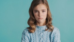 Upset blond teenage girl feeling sad because of bad marks at school posing isolated on blue background. Offended girl
