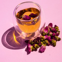 Tea with rosebuds. Dry rose buds, a teacup on a pink background. dried rose buds on a pink surface. Pink Dried Rose Buds Herbal Tea in a glass mug. close-up of tea with dried rose buds. 