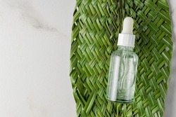 Beauty face oil with drops pipette on marble background. Grean tropical leaf decoration. Professional bottle for facial and body treatment. Skin care daily routine
