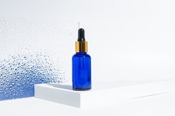 blue glass cosmetic bottle with a dropper on a white background with blue gradient. Natural cosmetics concept, natural essential oil and skin care products.