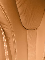 Modern luxury car brown leather interior. Part of orange perforated leather car seat details with white stitching. Interior of prestige car. Comfortable perforated leather seats. Perforated leather.