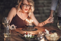 Beautiful happy Caucasian blonde woman blowing candles on birthday cake.