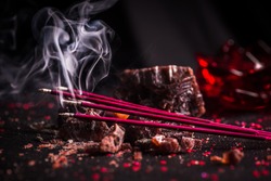 Red colored incense sticks burning against a dark background made up of natural black rock salt