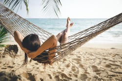 Summer vacations concept, Happy woman with white bikini, hat and shorts Jeans relaxing in hammock on tropical beach at sunset, Koh mak, Thailand
