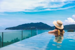 Summer travel vacation concept, Happy traveler asian woman with hat and bikini relax in luxury infinity pool hotel resort at day in Phuket, Thailand