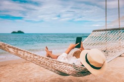 Summer travel vacation concept, Happy traveler asian woman using mobile phone and relax in hammock on beach in Koh Chang, Trad, Thailand