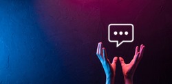 Hand on neon background holding a message icon, bubble talk notification sign in his hands. Chat icon, sms icon, comments icon, speech bubbles.