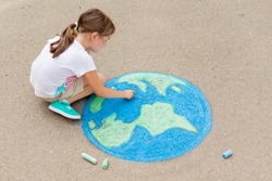 Kids play outdoors. Child girl draws a planet globe with a map of the world colored chalk on the pavement, asphalt. Earth, peace day concert.