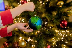 Close-up of little girl hanging Xmas glass bauble decoration ornament globe planet earth on christmas tree.  Merry christmas and new year concept. Selective focus