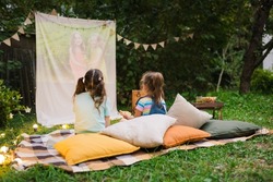 Backyard Family outdoor movie night with kids. Sisters spending time together and watching cimema at backyard. DIY Screen with film. Summer outdoor weekend activities with children. Open air cinema.