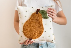Close-up of woman hands holding pillow. Punch needle embroidery pillow diy. Product is made according to the technique pushing woolen threads on foundation fabric with needle with wood handle