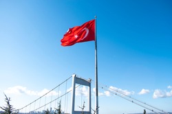Big Turkish flag in blue sky. Turkish flag rippling in the wind. The giant Turkish flag attached to the big post in front of the Fatih Sultan Mehmet Bridge.