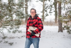 Man in red plaid jacket walking through the snow carrying firewood