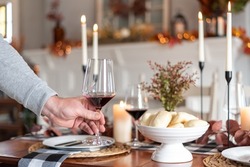 Man setting a glass of red wine on a holiday dinner table decorated for autumn