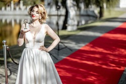 Portrait of a beautiful woman in white dress as a well-known actress holding famous movie award on the red carpet outdoors