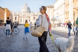 Stylish woman walks with a dog on the street on background of saint Peter's cathedral in Rome. Concept of italian lifestyle and travel