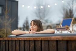 Young woman bathing in hot tub at mountains during winter. Concept of rest and recovery in hot vat. Idea of escape and recreation in mountains
