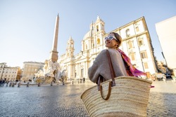 Woman walks on Navona square in Rome city on a sunny day. Female person with bag and colorful shawl in hair. Concept of italian lifestyle and travel