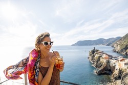 Woman enjoys summer cocktail and beautiful landscape of mediterranean coast in Vernazza village. Traveling famous Cinque Terre towns in northwestern Italy. Idea of summer vacation