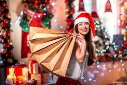 Young woman with shopping bags with Christmas decorations, candles, gifts and lights on bachground. Christmas sale