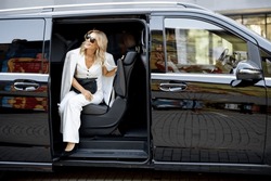Elegant business lady in white looks out of a minivan taxi. Concept of business trips and transportation