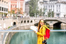 Young female traveler in yellow sweater and sunglasses standing with map on the bridge in the center of Ljubljana city in Slovenia. Traveling Slovenia