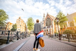 Young woman tourist standing back with dutch flag on the bridge enjoying beautiful morning view on the old town of Amsterdam city