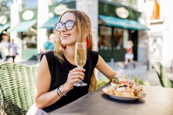 Young woman enjoying tasty appetizer with pinchos, traditional spanish snack, and glass of wine sitting outdoors at the bar in Valencia city