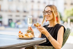 Young woman enjoying tasty appetizer with pinchos, traditional spanish snack, with glass of wine sitting outdoors at the bar in Valencia city
