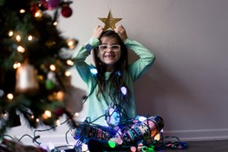 A young girl with glasses is decorating a Christmas tree and is happily playing with the decorations.