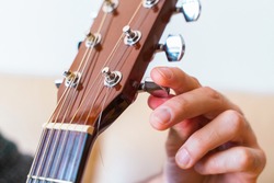 Detail of guitar tuned by turning the pegs on the neck. Unrecognizable man explaining step by step instructions to properly tune guitar strings. Music course online concept. Indoor lifestyles.