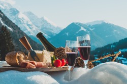 Traditional Italian food and drink outdoor in sunny winter day. Romantic alpine picnic in Dolomites with mountains background, Lambrusco cheese baguette and ham on the snow.