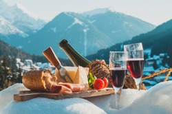 Traditional Italian food and drink outdoor in sunny winter day. Romantic alpine picnic in Dolomites with mountains background, Lambrusco cheese baguette and ham on snow.