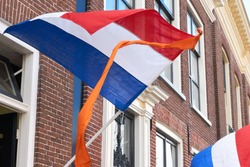 Dutch flags with orange streamer waving in the wind on facades of typical dutch houses on Koningsdag in the Netherlands. A national holiday in the Kingdom of the Netherlands                