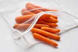Orange carrots in sustainable grocery mesh bag. Vegetables in reusable eco friendly packaging on light background. Zero waste shopping, plastic free, stop pollution, ecological concept.