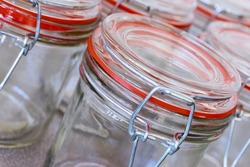 Closeup of empty glass canning jars or preserving containers with orange sealing ring in a row. Preserving food concept.