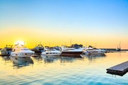 Luxury yachts docked in sea port at sunset. Marine parking of modern motor boats and blue water. Relaxation and fashionable vacation.