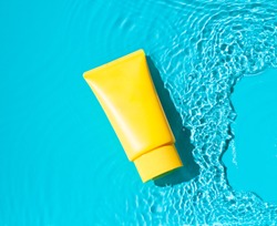 Sun cream yellow tube on the blue water surface. Summer vacation  cosmetics concept. Top view