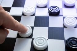 Board game of checkers. Black and white chips for the game. Chess field. Checkers move close-up. Checker in hand.