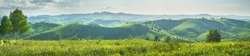 Panoramic view of a summer evening in the mountains, green meadows, mountain slopes and hills