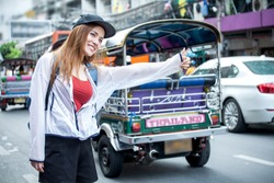 beautiful Young Asian women tourist traveler smiling with backpack on the Traffic Road raising hand calling cab in China town Yaowarat city bangkok thailand . girl waiting for a taxi car bus,tuk tuk
