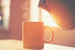 kettle pouring boiling water into a cup in morning sunlight