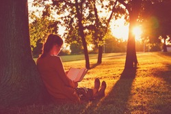 girl reading book at park in summer sunset light