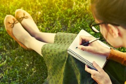 girl with pen writing on notebook on grass outside
