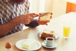 male hands spreading butter on toasted bread while morning breakfast