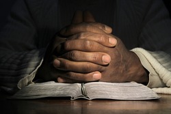man praying with hand on bible black background stock photo