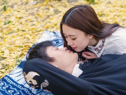 Portrait of couple of Chinese young people lying on autumn ground covered with golden ginkgo leaves,  prepare to kiss, full of love, lover concept.