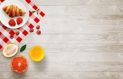 Fruit breakfast with free space on wooden table. Croissant, orange, strawberries, raspberries, lemon, juice, with top view.