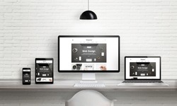 Creative web design agency presentation on multiple devices. Computer display, laptop, tablet, smart phone on white wooden desk. Brick white wall in background.