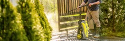 Unrecognizable man cleaning a wooden gate with a power washer. High pressure water cleaner used to DIY repair garden gate. Web banner.